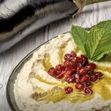 Moutabal, a smoky Lebanese aubergine dip with tahini, topped with olive oil, pomegranate seeds and fresh mint, next to a whole aubergine at Falafoliva