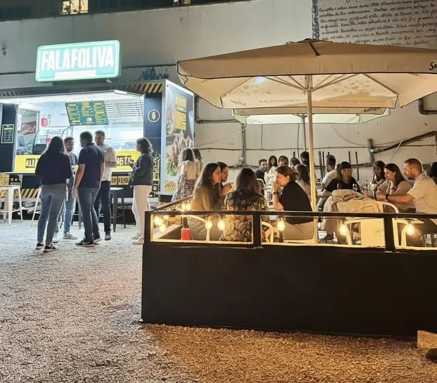 The Falafoliva truck lit up at night with a crowd of guests